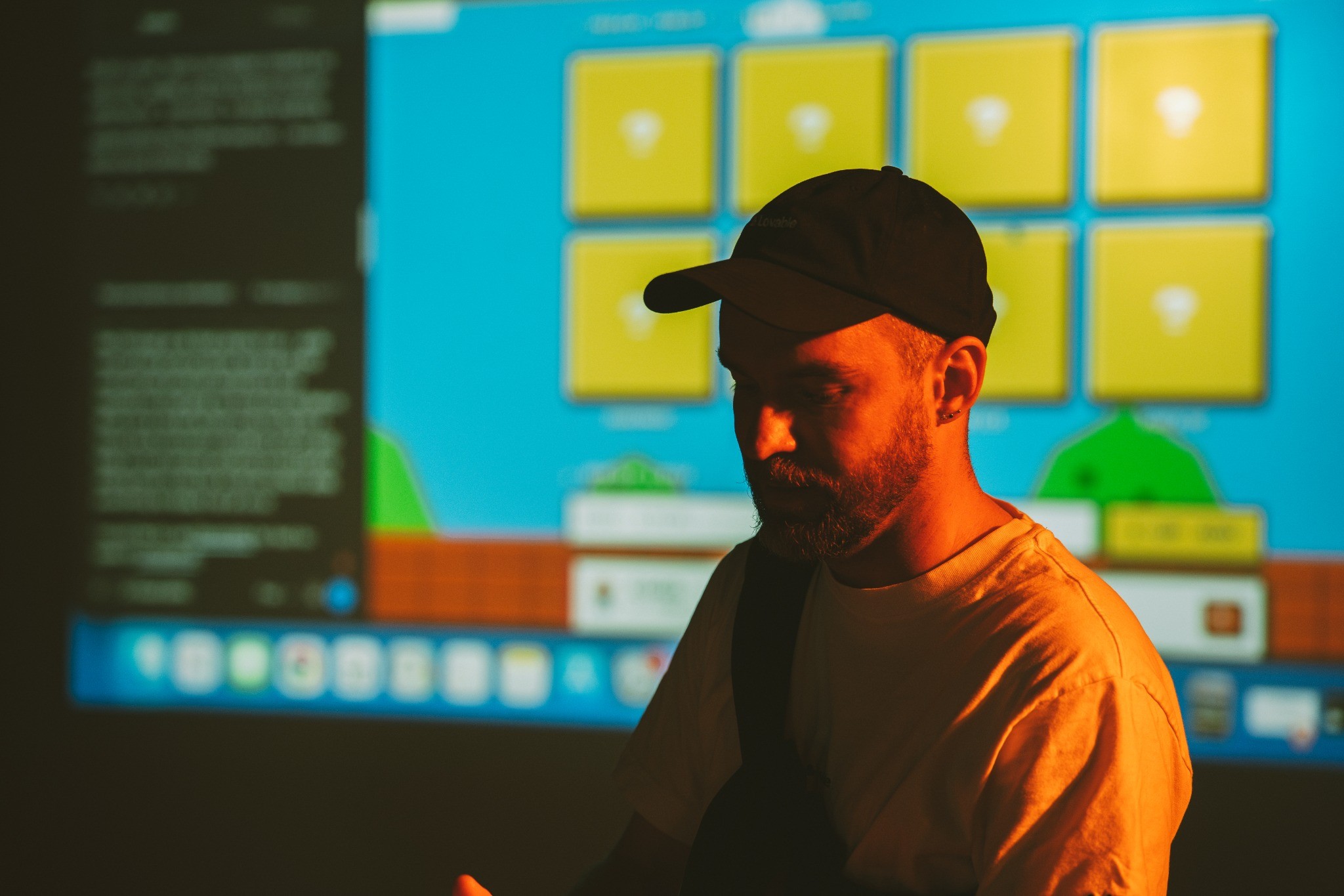A builder in a cap silhouetted against a cyan and amber product screen at the Wintercircus community gathering.